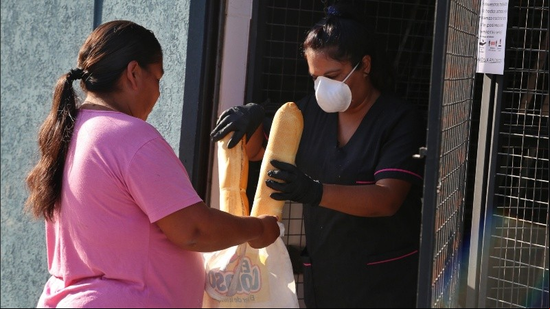 Una mujer con barbijo entrega pan a una vecina.